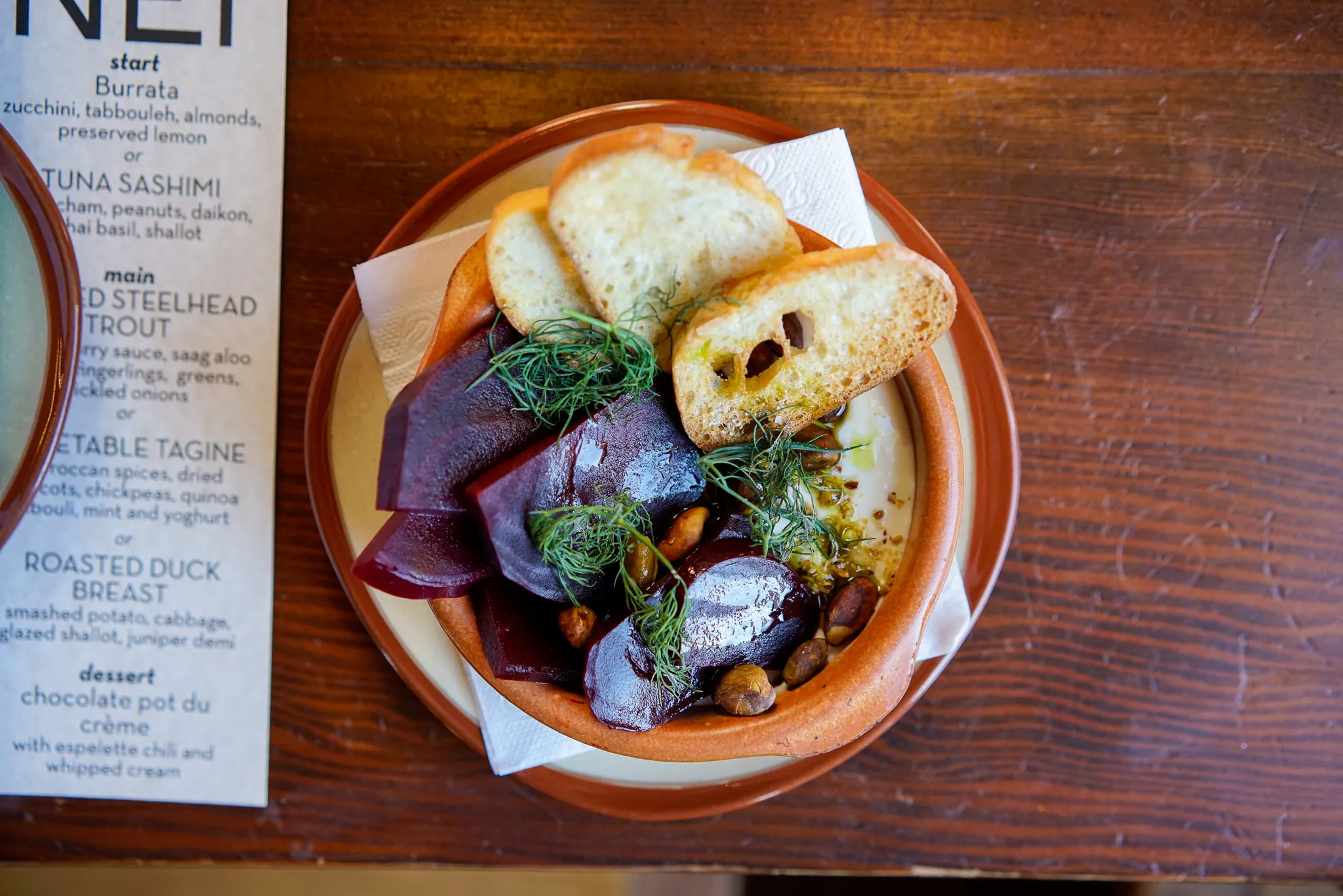 Sherry-marinated beets in a clay bowl with bread, on a wooden table at Perro Negro Taperia