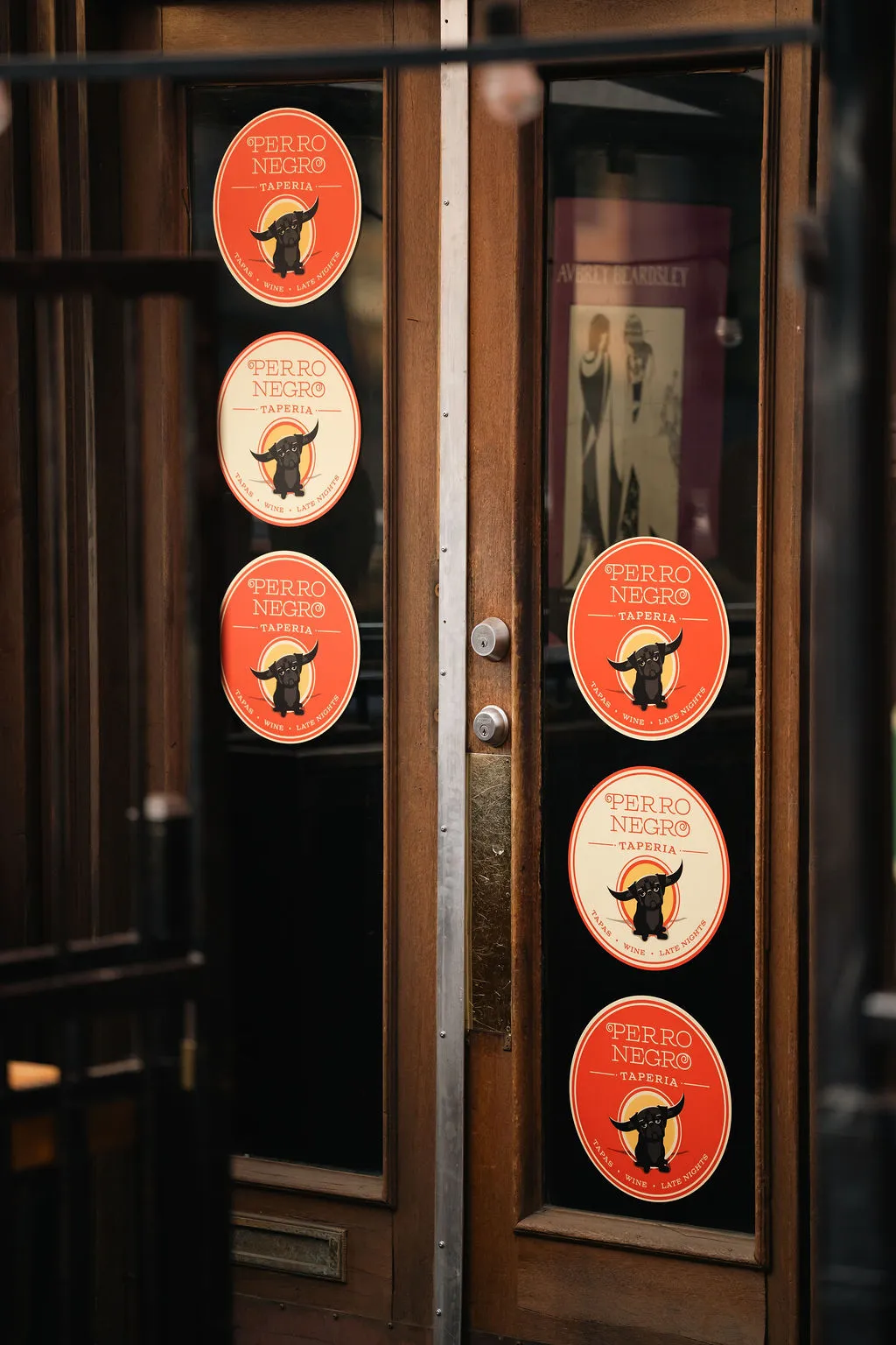 The entrance to Perro Negro Taperia — its door covered in coral coasters with the bulldog mark