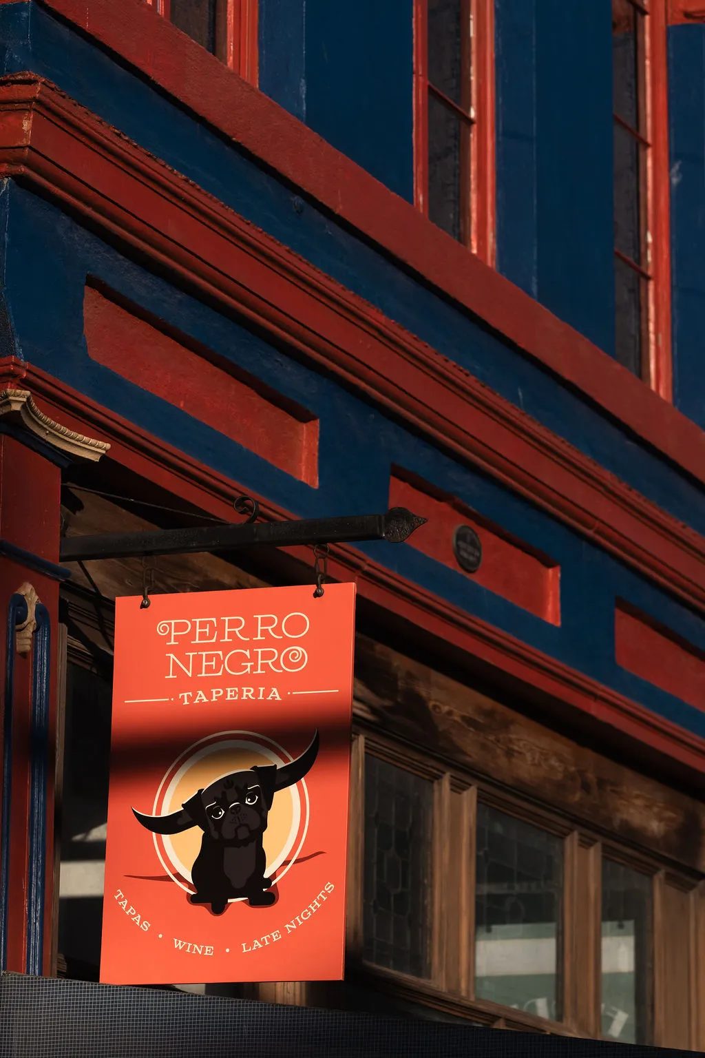 Perro Negro Taperia coral hanging sign against the navy and red Yates Street facade