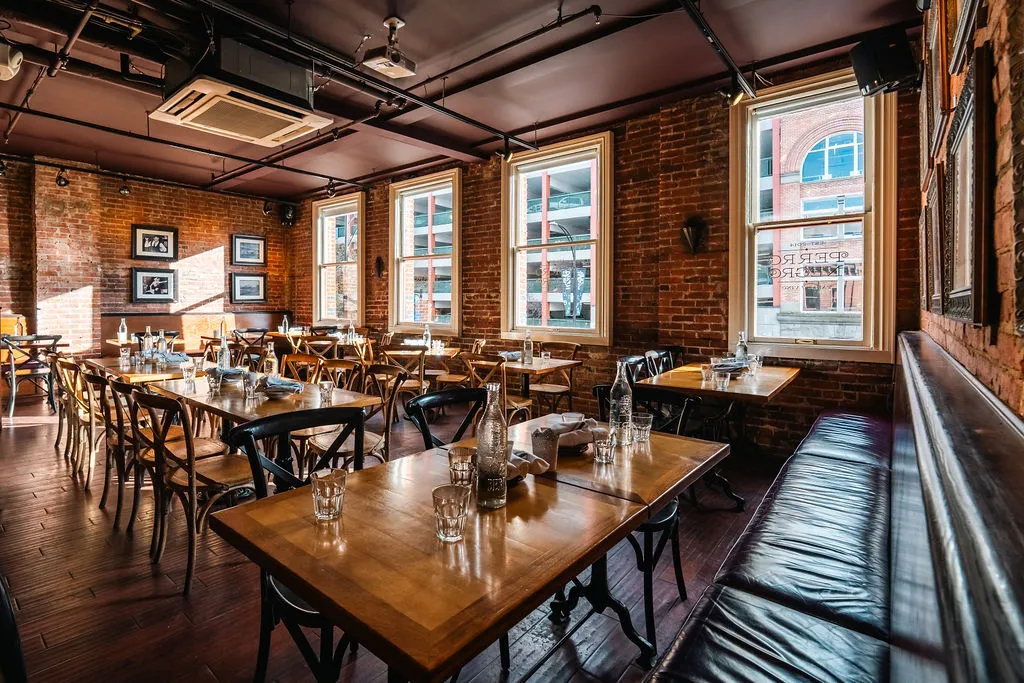 The dining room at Perro Negro Taperia, set for service — wood tables, leather banquette, big arched windows