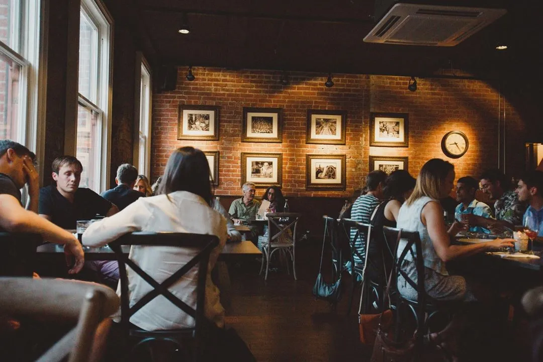 Guests filling the Perro Negro Taperia dining room mid-service — exposed brick, framed photos, and the room's big clock