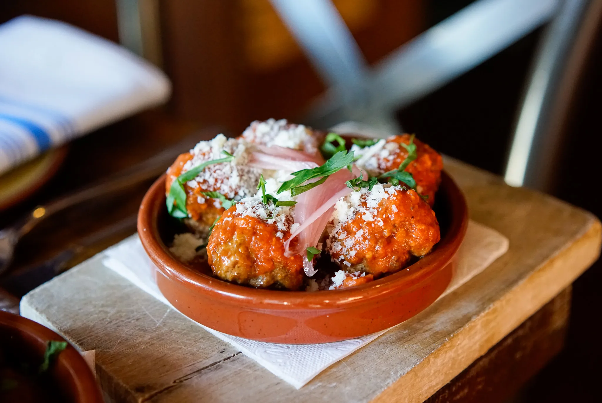 Catalan meatballs in a terracotta bowl, topped with parmesan and pickled red onion