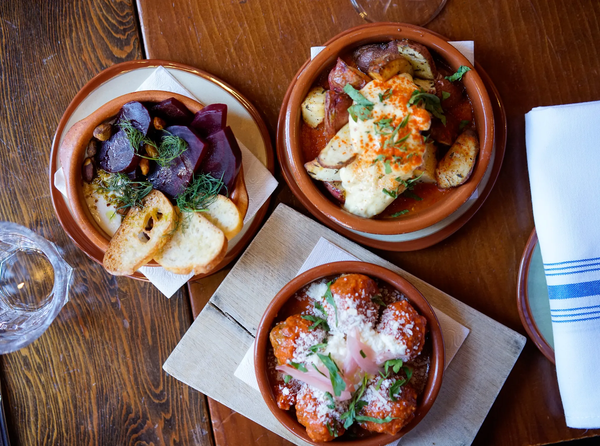 A spread of tapas on the wooden table at Perro Negro Taperia, plates arriving in waves